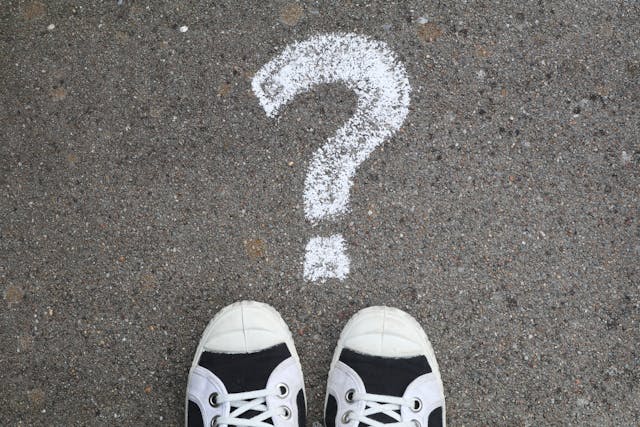 photograph of black and white sneakers on black pavement next to question mark drawn with white chalk